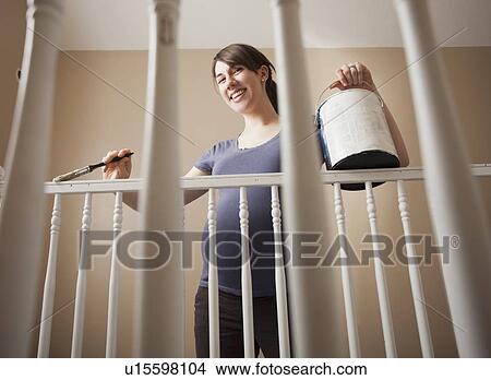 Picture - Low angel view of young woman painting balustrade. Fotosearch