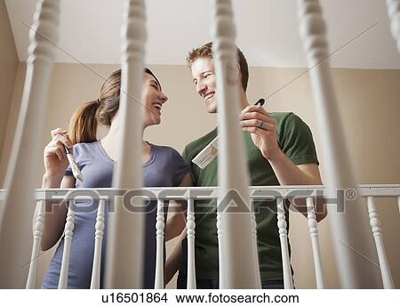 Picture - Low angle view of young couple standing face to face holding paint brush. Fotosearch