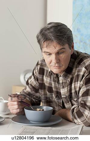 Stock Photograph - Man eating breakfast and reading newspaper. Fotosearch