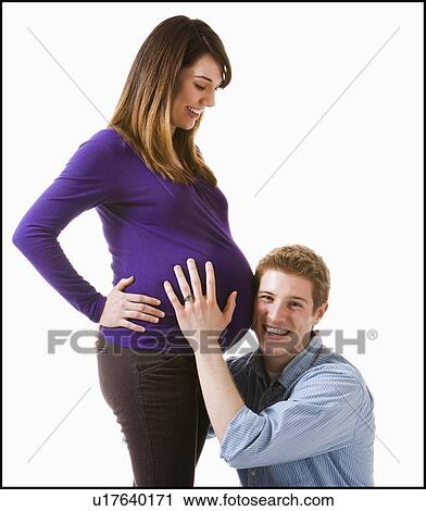Stock Image - Man embracing pregnant woman, studio shot. Fotosearch