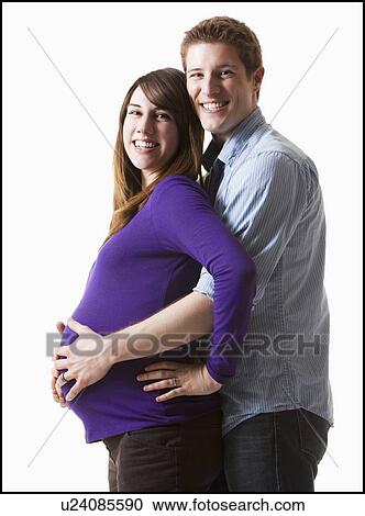 Stock Image - Man embracing pregnant woman, studio shot. Fotosearch