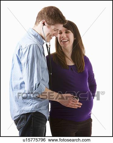 Stock Photograph - Man listening of heartbeating on belly of pregnant woman, studio shot. Fotosearch