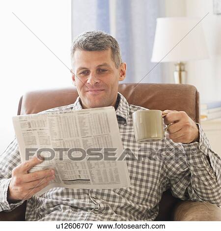Stock Photo - Man sitting in living room with newspaper and mug. Fotosearch