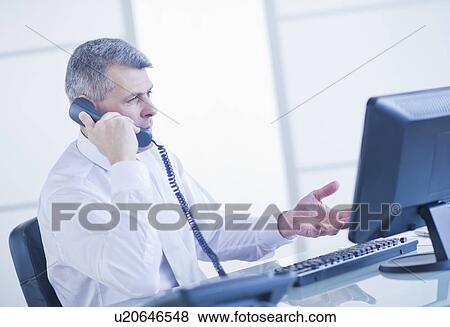 Stock Photo - Man sitting in office and talking on landline phone. Fotosearch