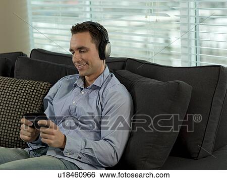 Man sitting on sofa listening music View Large Photo Image Stock Photograph - Man sitting on sofa listening music. Fotosearch