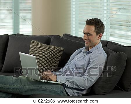 Man sitting on sofa using computer View Large Photo Image Stock Photography - Man sitting on sofa using computer. Fotosearch