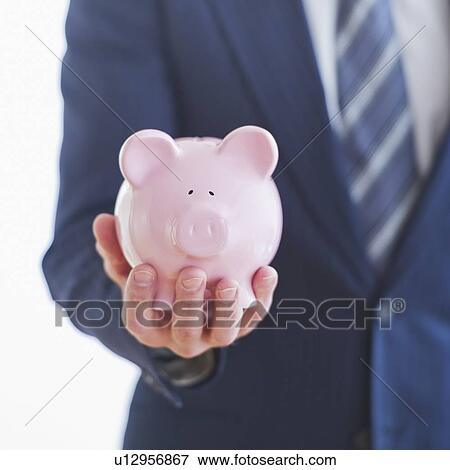 Stock Photo - Man wearing suit holding piggybank. Fotosearch