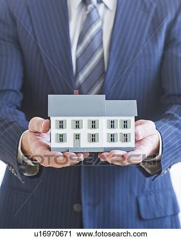Man wearing suit holding small house model View Large Photo Image Stock Image - Man wearing suit holding small house model. Fotosearch