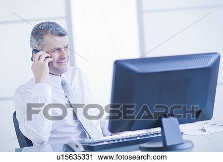 Man with mobile phone sitting in office View Large Photo Image Stock Image - Man with mobile phone sitting in office. Fotosearch