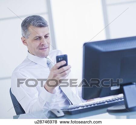 Man with mobile phone sitting in office View Large Photo Image Stock Photo - Man with mobile phone sitting in office. Fotosearch