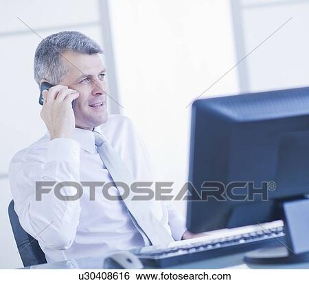 Stock Photograph - Man with mobile phone sitting in office. Fotosearch