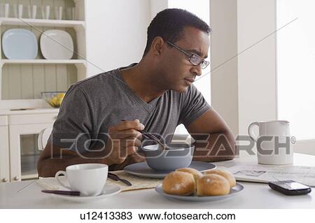 Stock Image - Mature man eating breakfast and reading newspaper. Fotosearch