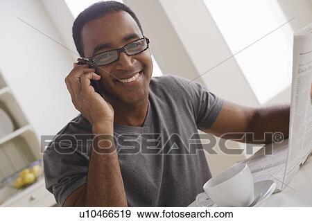 Stock Photo - Mature man talking via mobile while holding newspaper. Fotosearch