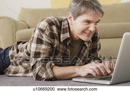 Stock Image - Mature man using laptop at home. Fotosearch
