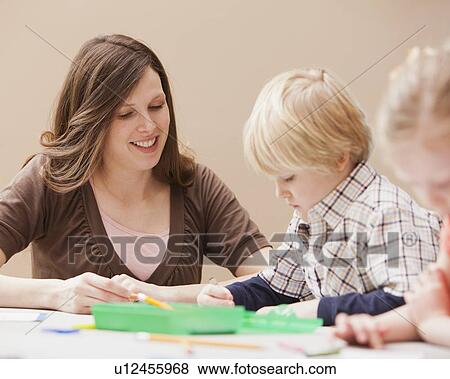 Mid adult woman teaching boy (4-5) drawing in kindergarten View Large Photo Image Stock Photo - Mid adult woman teaching boy (4-5) drawing in kindergarten. Fotosearch
