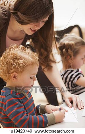 Stock Photo - Mid adult woman teaching boy (4-5) drawing in kindergarten. Fotosearch