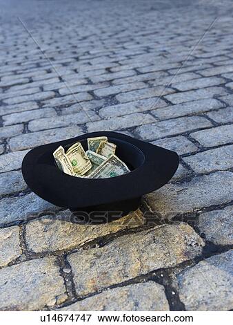 Stock Photo - Money in hat on cobblestone street. Fotosearch