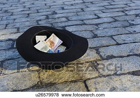 Stock Photo - Money in hat on cobblestone street. Fotosearch
