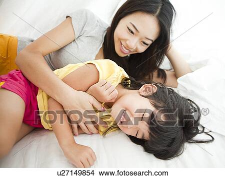 Mother with daughter lying down in bed, tickling (4-5) View Large Photo Image Picture - Mother with daughter lying down in bed, tickling (4-5). Fotosearch