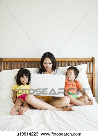 Mother with daughters (2-3, 4-5) sitting on bed, using laptop View Large Photo Image Stock Image - Mother with daughters (2-3, 4-5) sitting on bed, using laptop. Fotosearch