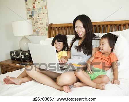 Mother with daughters (2-3, 4-5) sitting on bed, using laptop View Large Photo Image Stock Photo - Mother with daughters (2-3, 4-5) sitting on bed, using laptop. Fotosearch