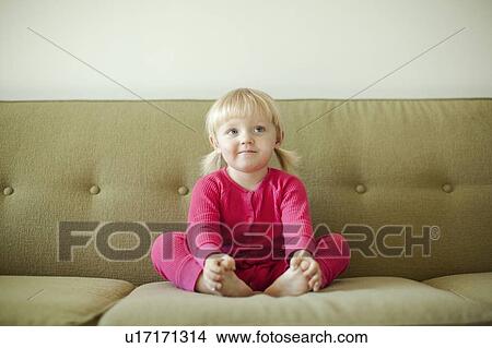Picture - Portrait of baby girl (18-23 months) sitting on sofa. Fotosearch
