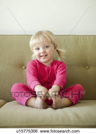 Stock Photograph - Portrait of baby girl (18-23 months) sitting on sofa. Fotosearch