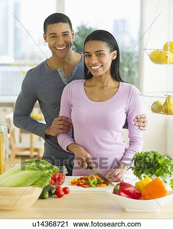 Stock Image - Portrait of couple chopping vegetables in kitchen. Fotosearch