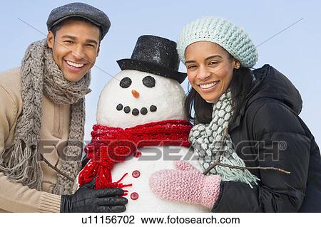 Stock Image - Portrait of couple with snowman. Fotosearch