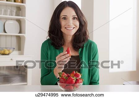 Stock Photography - Portrait of mature woman with strawberries on table. Fotosearch