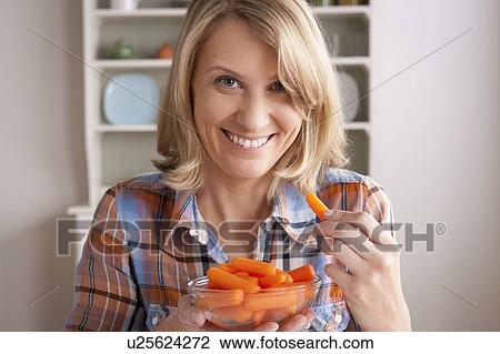 Stock Image - Portrait of mid adult woman with bowl of carrots. Fotosearch