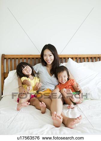 Portrait of mother with daughters (2-3, 4-5) sitting on bed View Large Photo Image Stock Photograph - Portrait of mother with daughters (2-3, 4-5) sitting on bed. Fotosearch