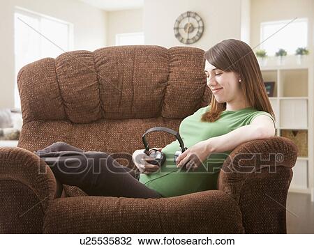 Portrait of pregnant woman sitting on sofa with headphones on her belly View Large Photo Image Stock Image - Portrait of pregnant woman sitting on sofa with headphones on her belly. Fotosearch