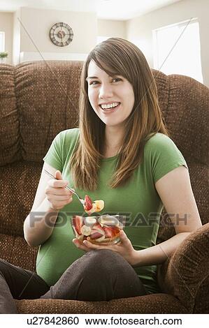 Portrait of pregnant woman sitting on sofa and eating salad View Large Photo Image Stock Image - Portrait of pregnant woman sitting on sofa and eating salad. Fotosearch