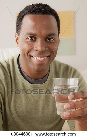 Stock Image - Portrait of smiling man holding glass of water. Fotosearch