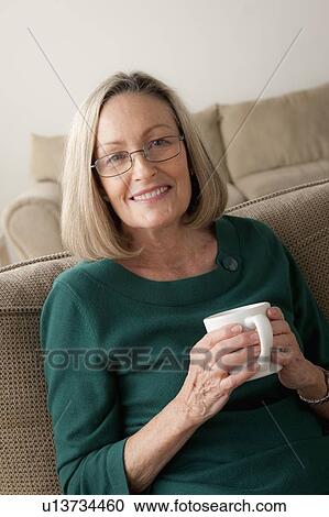 Portrait of smiling woman sitting on sofa and holding mug View Large Photo Image Stock Image - Portrait of smiling woman sitting on sofa and holding mug. Fotosearch