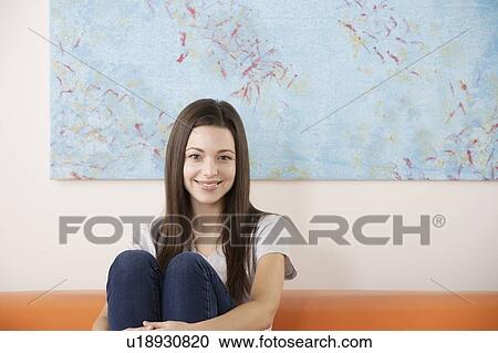 Stock Image - Portrait of smiling woman sitting on sofa. Fotosearch