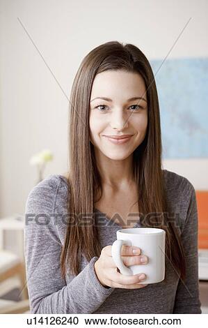 Stock Image - Portrait of smiling young woman holding mug. Fotosearch