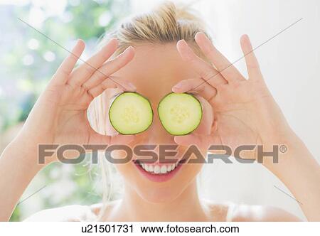 Stock Image - Portrait of smiling young woman covering eyes with slices of cucumber. Fotosearch