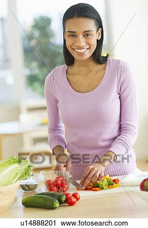 Stock Image - Portrait of woman chopping vegetables in kitchen. Fotosearch