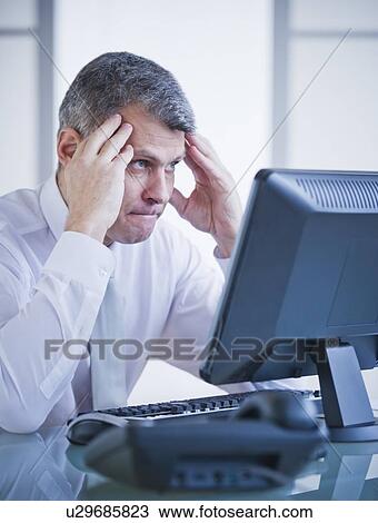 Stock Image - Portrait of worried businessman working at desk. Fotosearch