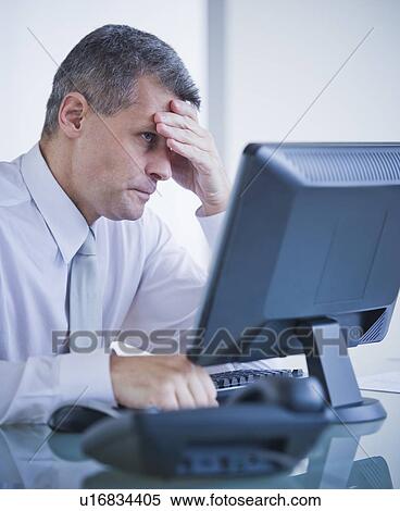 Stock Photography - Portrait of worried businessman working at desk. Fotosearch