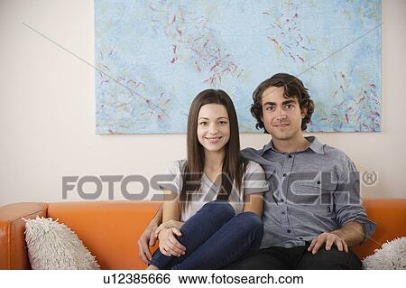 Portrait of young couple sitting on sofa View Large Photo Image Stock Photograph - Portrait of young couple sitting on sofa. Fotosearch