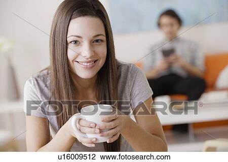 Portrait of young woman holding mug, man in background View Large Photo Image Stock Image - Portrait of young woman holding mug, man in background. Fotosearch