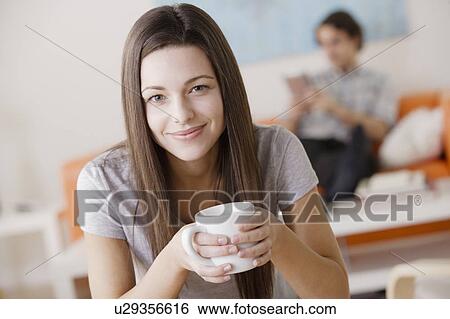 Stock Photograph - Portrait of young woman holding mug, man in background. Fotosearch