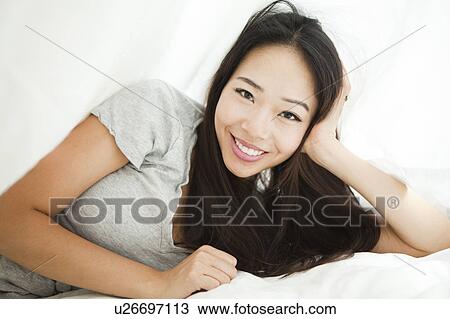 Stock Image - Portrait of young woman lying on side with hand on chin. Fotosearch