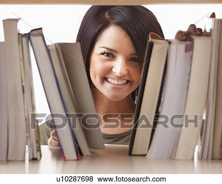 Stock Photo - Portrait of young woman searching book on shelf. Fotosearch