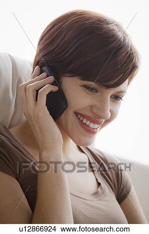 Picture - Portrait of young woman sitting on armchair and talking via mobile. Fotosearch