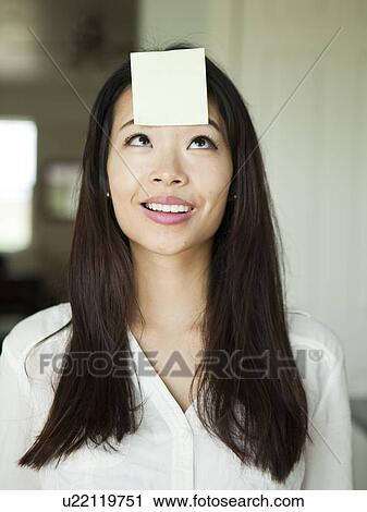 Stock Image - Portrait of young woman with adhesive note stuck to her forehead. Fotosearch