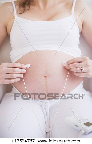 Pregnant woman holding earbuds on her belly View Large Photo Image Stock Photo - Pregnant woman holding earbuds on her belly. Fotosearch